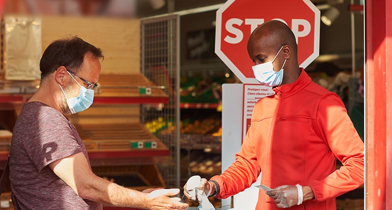 customer getting hands sanitized by employee before entering retail store during COVID 19 pandemic