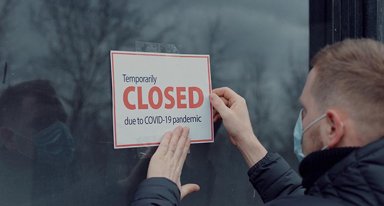 man posting a sign that say closed due to COVID-19 pandemic