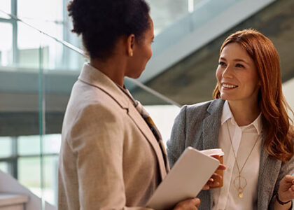 Happy entrepreneur talking to her African American female colleague while drinking coffee in the office.