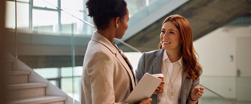 Happy entrepreneur talking to her African American female colleague while drinking coffee in the office.