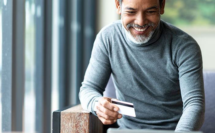 Older man smiling at his digital device while holding a credit card