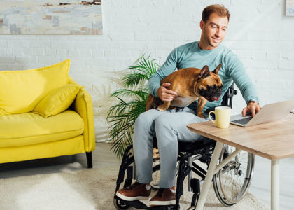 Man in a wheelchair works on his computer while his dog sits in his lap