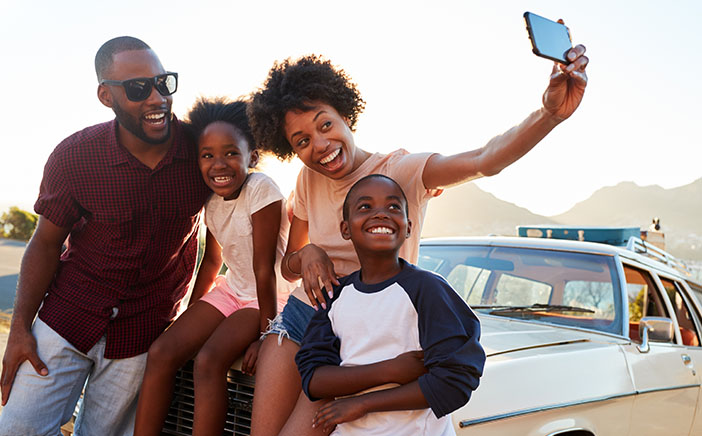 Happy Black family taking a selfie together on the hood of their car