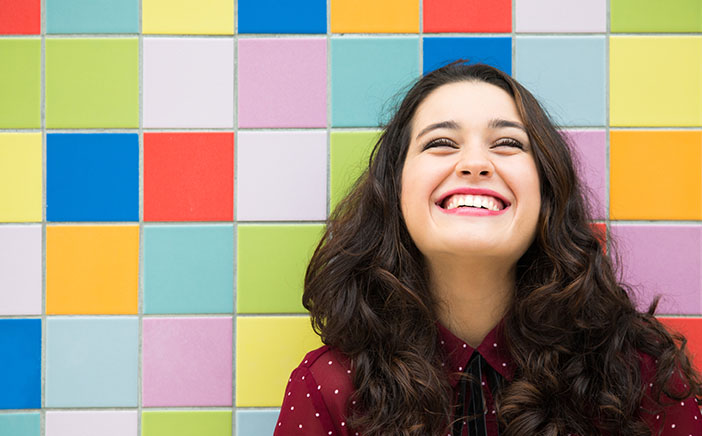 Woman with a big smile standing in front of a multicolor patterned wall