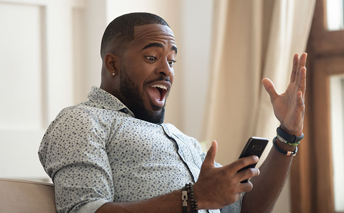 Black male surprised and delighted as he gazes at his phone