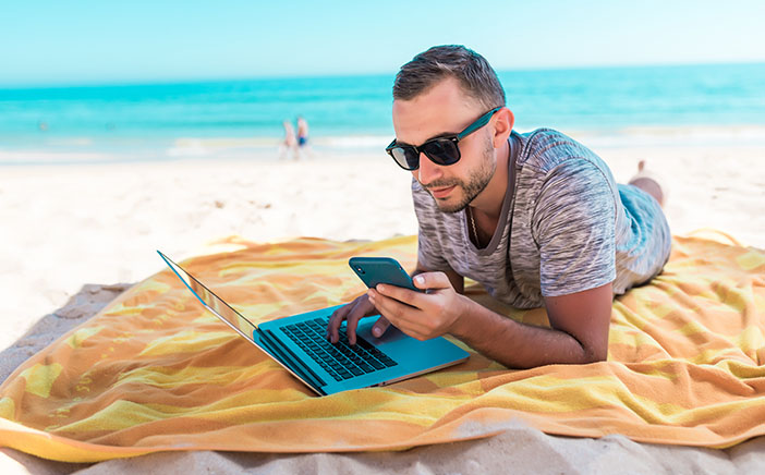 Man sitting on the beach with a laptop and phone