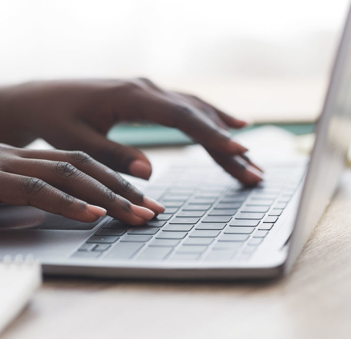 Closeup of black person's hands typing on laptop keyboard