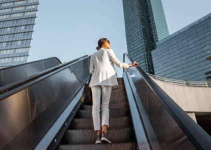 Stylish businesswoman in white suit going up on the escalator outdoors with skyscrapers