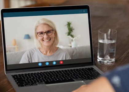 Laptop on a table that displays a virtual video call with an older woman wearing glasses