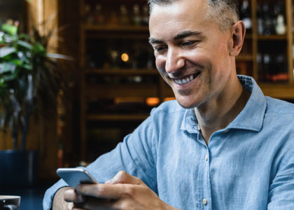 Middle-aged man smiles at his phone while sitting in a cafe