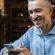Middle-aged man smiles at his phone while sitting in a cafe
