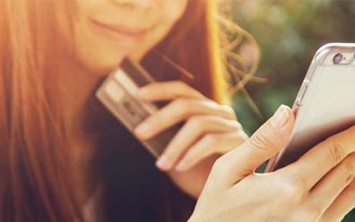 Young woman smiles as she holds smartphone in one hand and credit card in the other