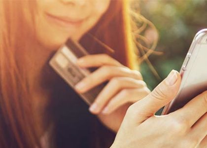 Young woman smiles as she holds smartphone in one hand and credit card in the other