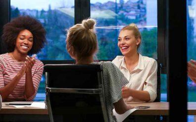 Young corporate individuals sit at a conference table and clap for one another in an office