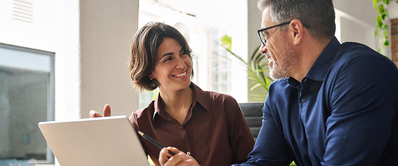 Two professional business people cheerfully discuss strategy in front of a laptop in an office setting.