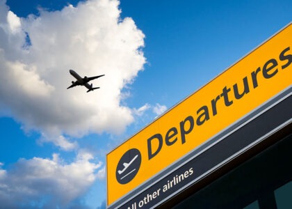 Airport departures sign with an airplane flying overhead