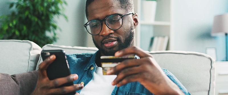 Black young man purchases with card from his mobile smart phone from the comforts of his home.