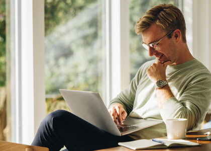 Competent CX talent smiles at his laptop in his home office