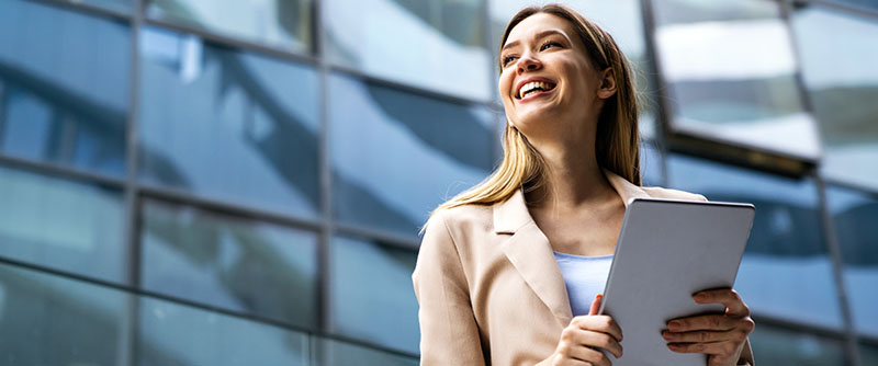 Female corporate leader looks optimistically into the horizon with a tablet in her hands outside of a building