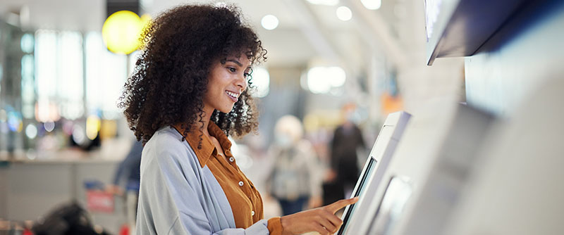 Happy customer at airport operates automatic ticket kiosk