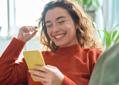 Young woman laughs at her phone as she sits on her couch at home