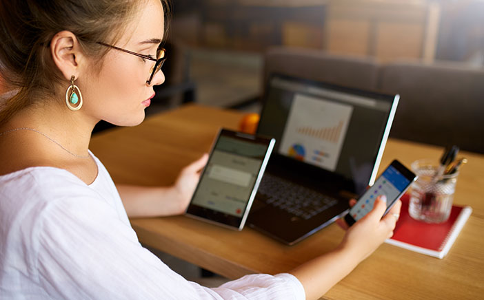 Young woman managing her techological devices across phone, tablet, and laptop
